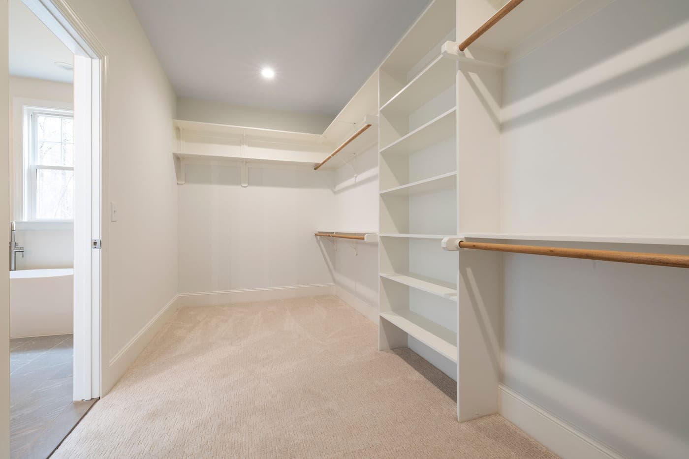A bright, empty walk-in closet with white shelving and hanging rods